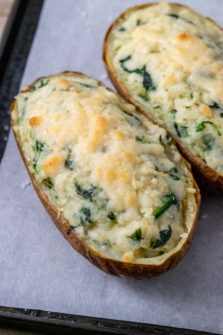 two potatoes filled with mashed potato, cream cheese, and spinach topped with parmesan cheese