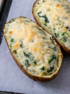 two potatoes filled with mashed potato, cream cheese, and spinach topped with parmesan cheese
