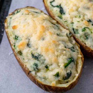 two potatoes filled with mashed potato, cream cheese, and spinach topped with parmesan cheese