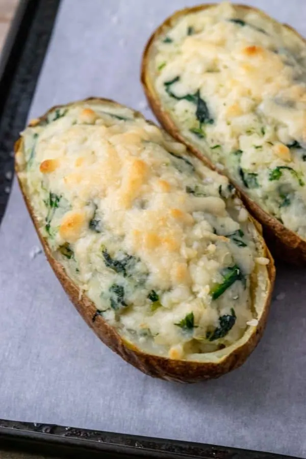 two potatoes filled with mashed potato, cream cheese, and spinach topped with parmesan cheese