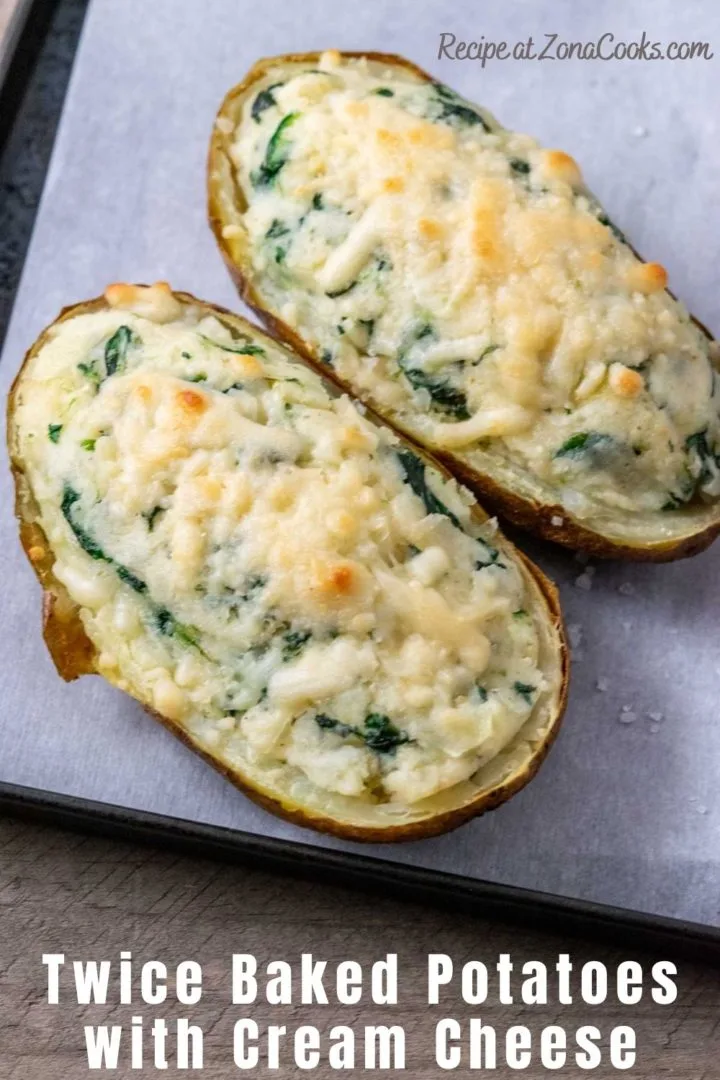 two twice baked potatoes with cream cheese and spinach on a baking sheet.