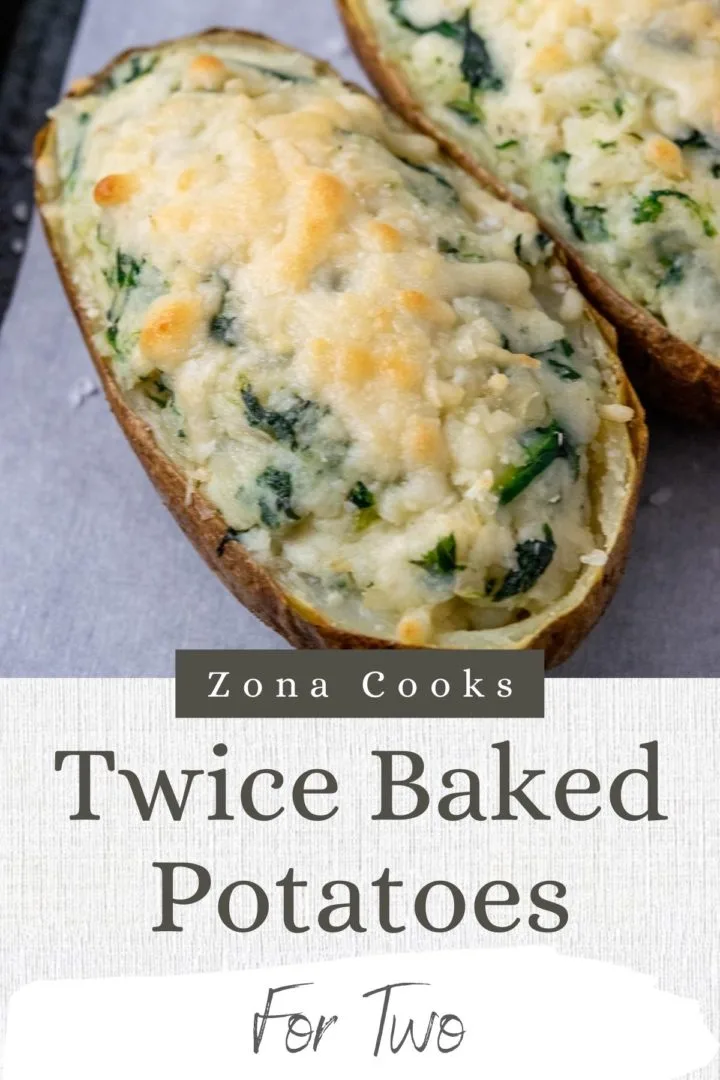 two twice baked potatoes with cream cheese and spinach on a baking sheet.