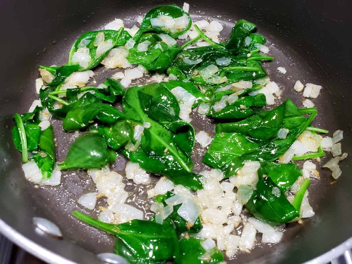 onions, garlic, and spinach leaves cooking in butter