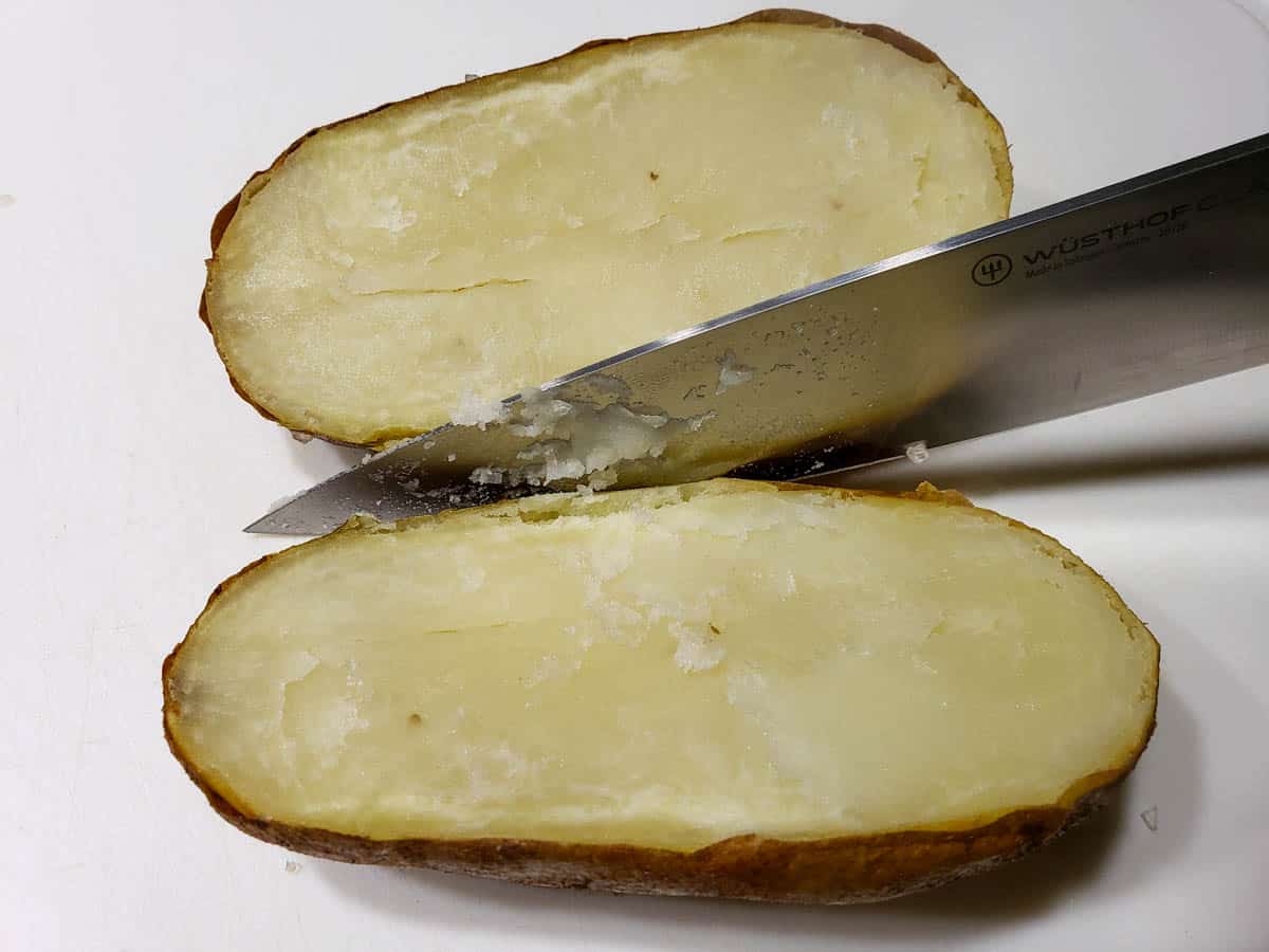 a potato with a chef knife cutting it in half