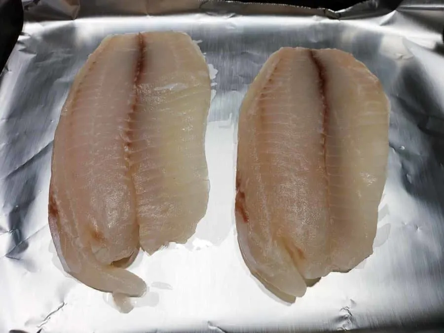 a baking sheet covered in tinfoil filled with two tilapia fish fillets