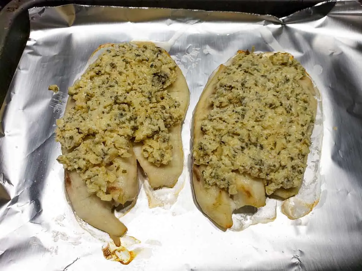 a baking sheet covered in tinfoil filled with two tilapia fish fillets topped with parmesan cheese and mayo mixture