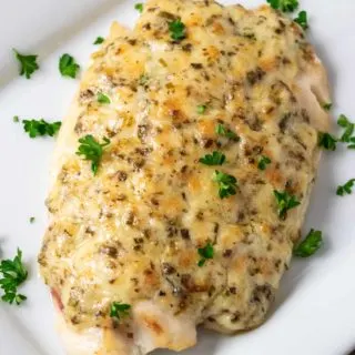 a plate filled with a piece of Tilapia fish topped with a Parmesan and mayo mixture and sprinkled with parsley