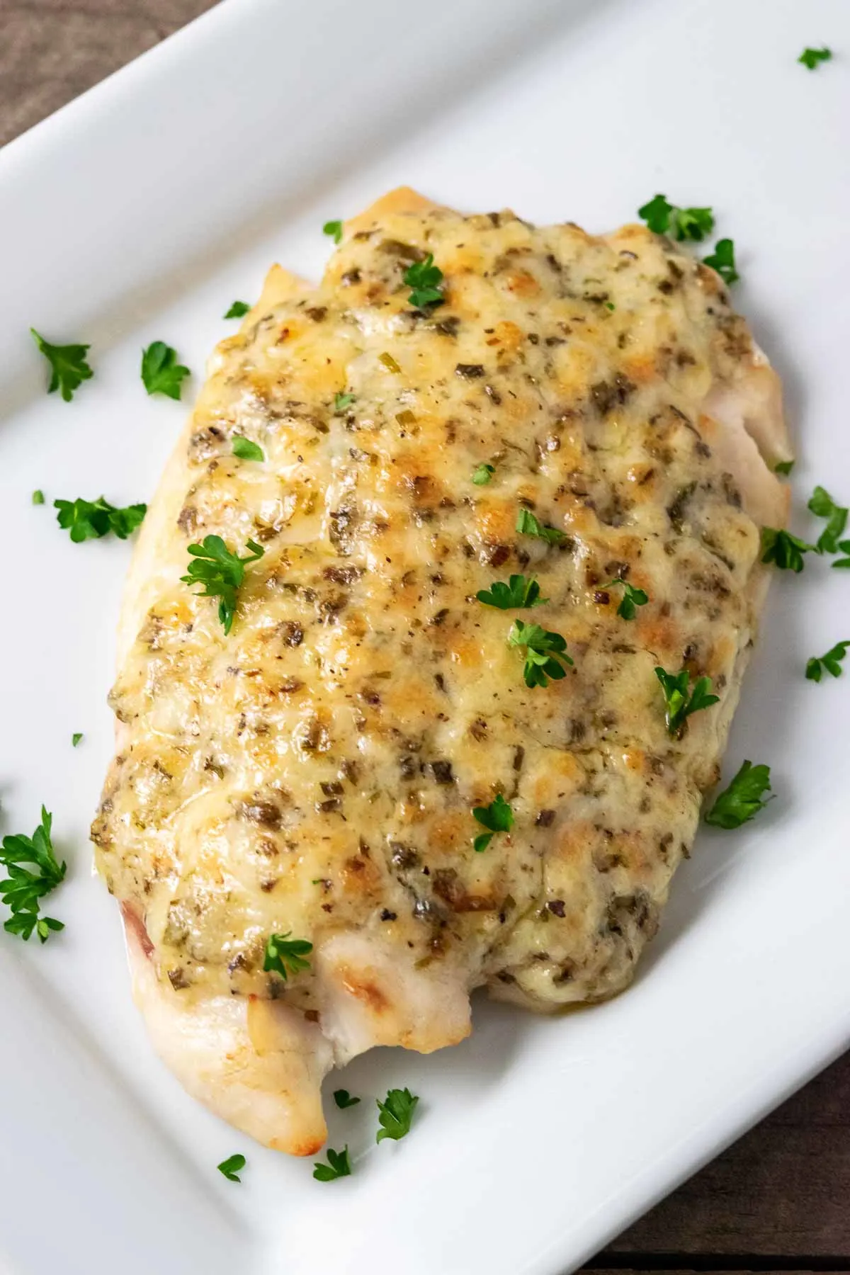 a plate filled with a piece of Tilapia fish topped with a Parmesan and mayo mixture and sprinkled with parsley