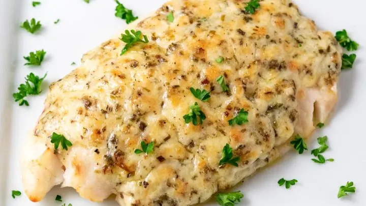 a plate filled with a piece of Tilapia fish topped with a Parmesan and mayo mixture and fresh parsley