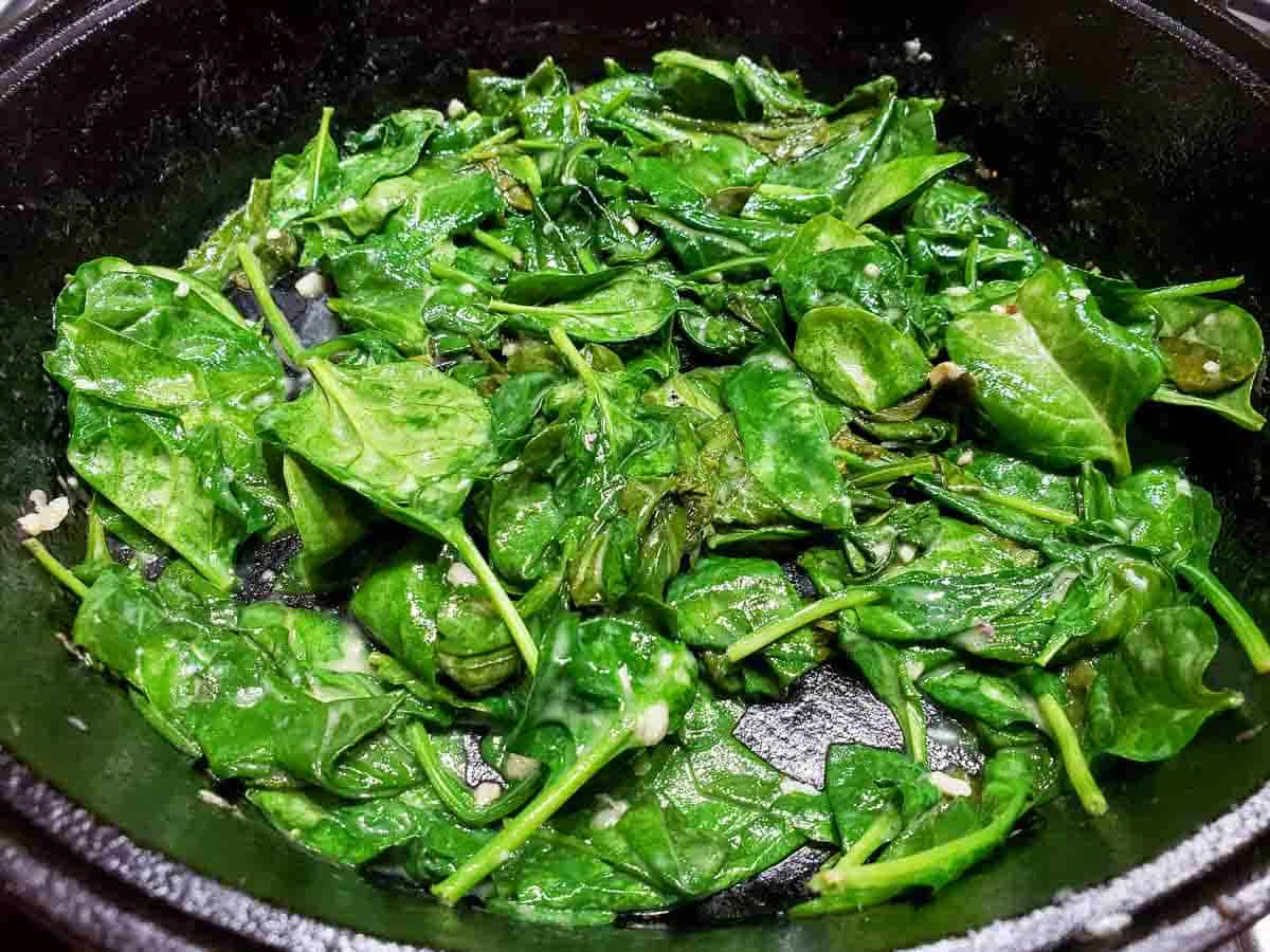 wilted spinach leaves cooking in a cast iron skillet