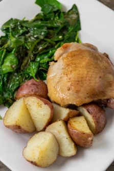 a plate with a golden brown chicken thigh with sides of red potatoes and spinach coated in sauce