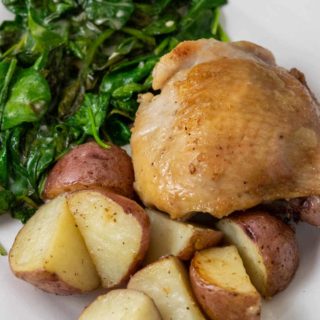 a plate with a golden brown chicken thigh with sides of red potatoes and spinach coated in sauce