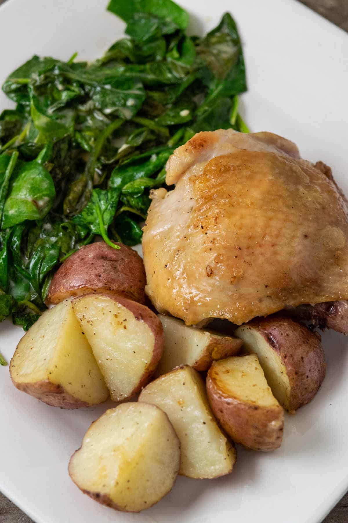 a plate with a golden brown chicken thigh with sides of red potatoes and spinach coated in sauce