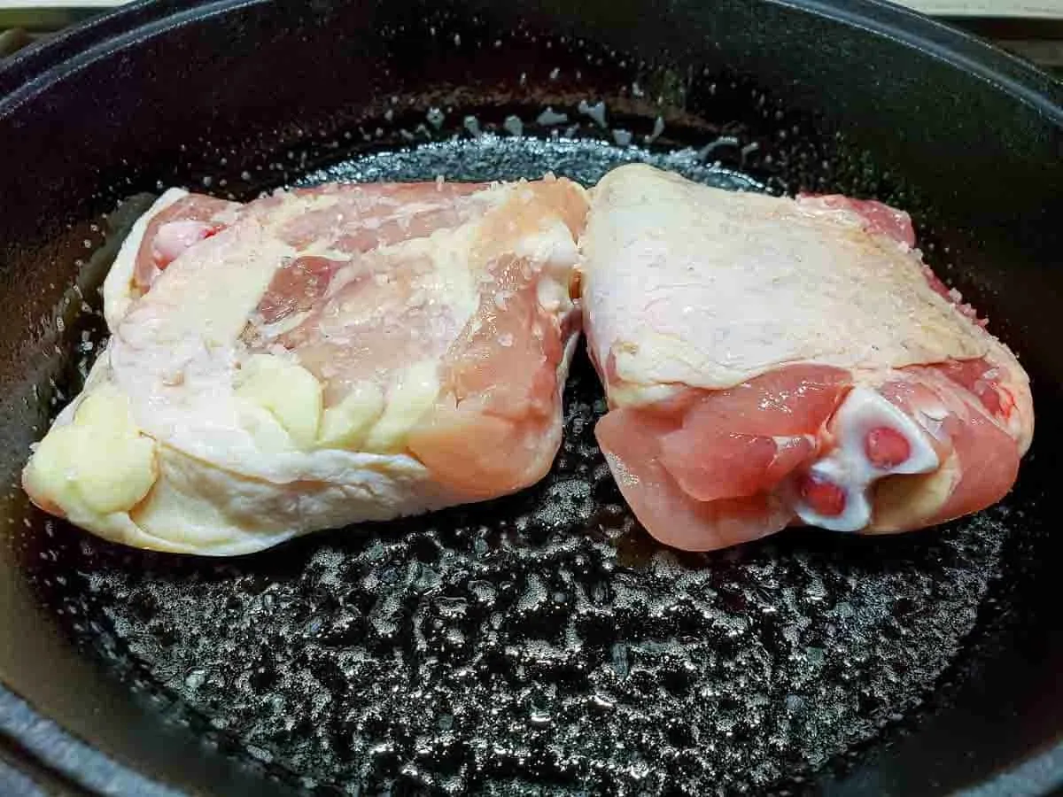 two chicken thighs cooking in a cast iron skillet