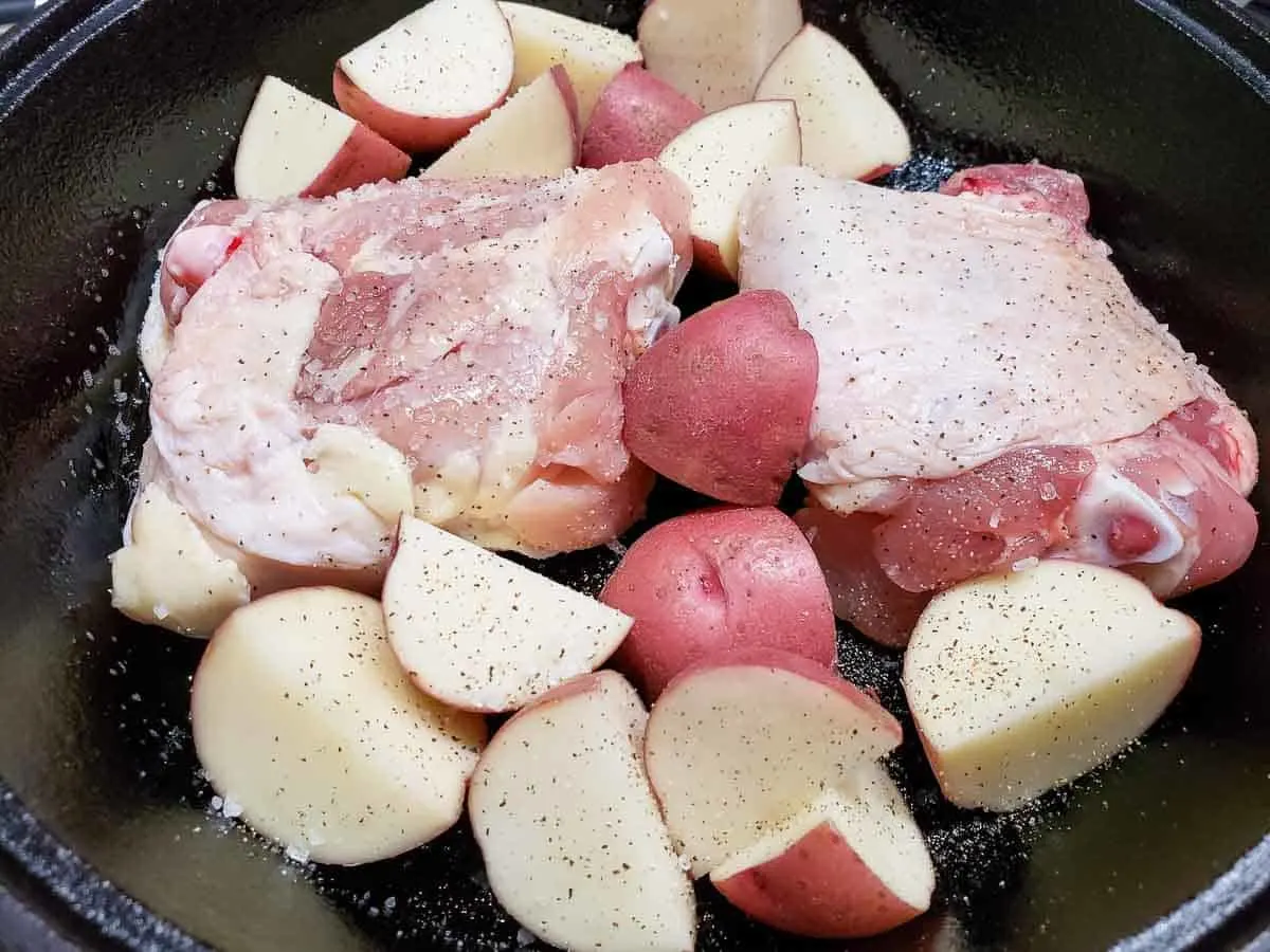 two chicken thighs and red skin potatoes cooking in a cast iron skillet