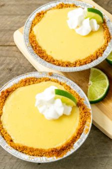 two small yellow pies in graham crusts topped with whipped cream and quarter lime slice.