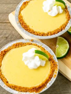 two small yellow pies in graham crusts topped with whipped cream and quarter lime slice.
