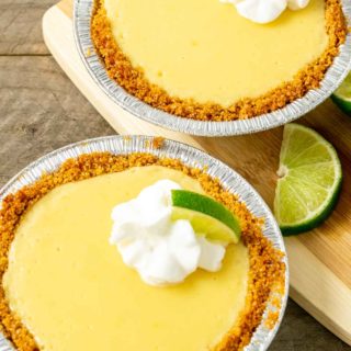 two small yellow pies in graham crusts topped with whipped cream and quarter lime slice.