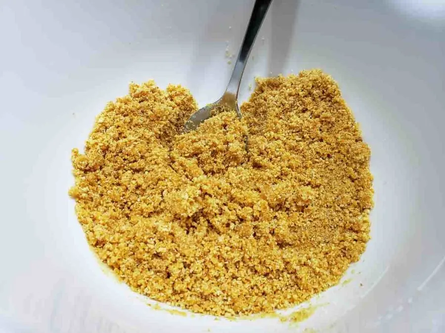 a bowl filled with graham crumbs mixed with melted butter.