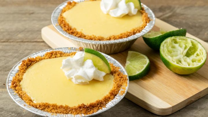 two mini yellow pies in graham crusts garnished with whipped cream and quarter lime slice