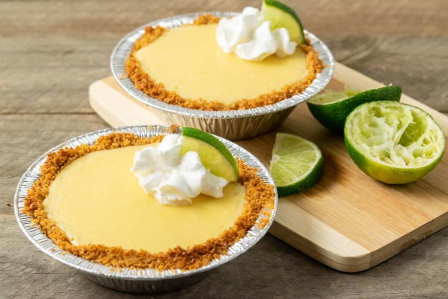 two mini yellow pies in graham crusts garnished with whipped cream and quarter lime slice.