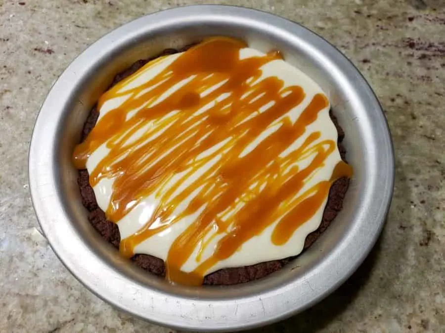 a small pie pan filled with chocolate crust, cream cheese filling, and caramel drizzle.