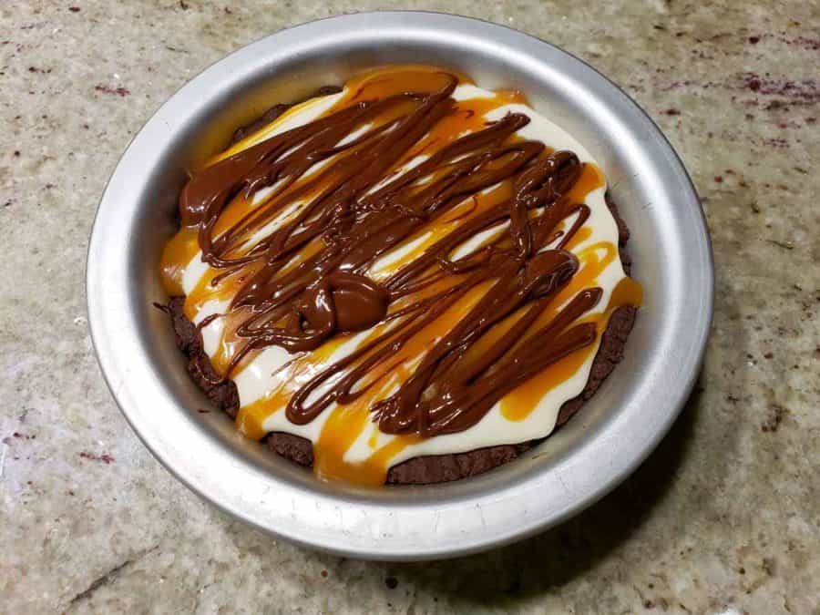 a small pie pan filled with chocolate crust, cream cheese filling, caramel drizzle, and chocolate ganache drizzle.