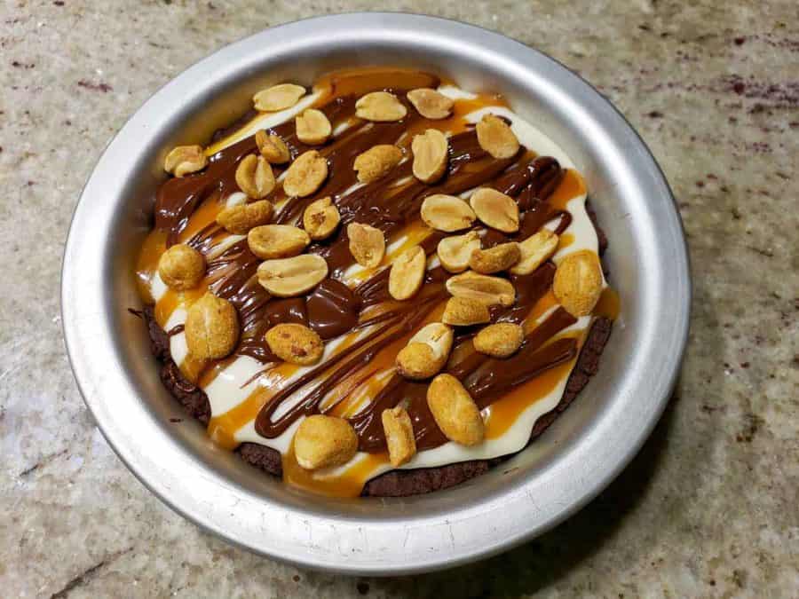 a small pie pan filled with chocolate crust, creamy filling, caramel sauce drizzle, chocolate ganache drizzle, and peanuts scattered over top.