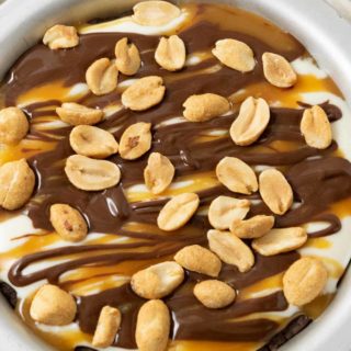 a top down view of a small pie pan filled with chocolate crust, creamy filling, caramel sauce drizzle, chocolate ganache drizzle, and peanuts.