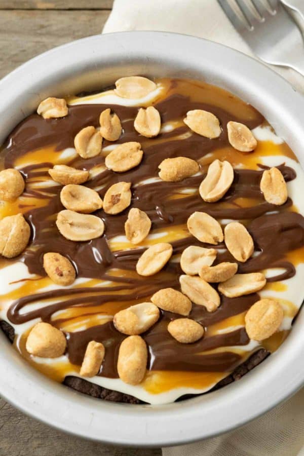 a top down view of a small pie pan filled with chocolate crust, creamy filling, caramel sauce drizzle, chocolate ganache drizzle, and peanuts.