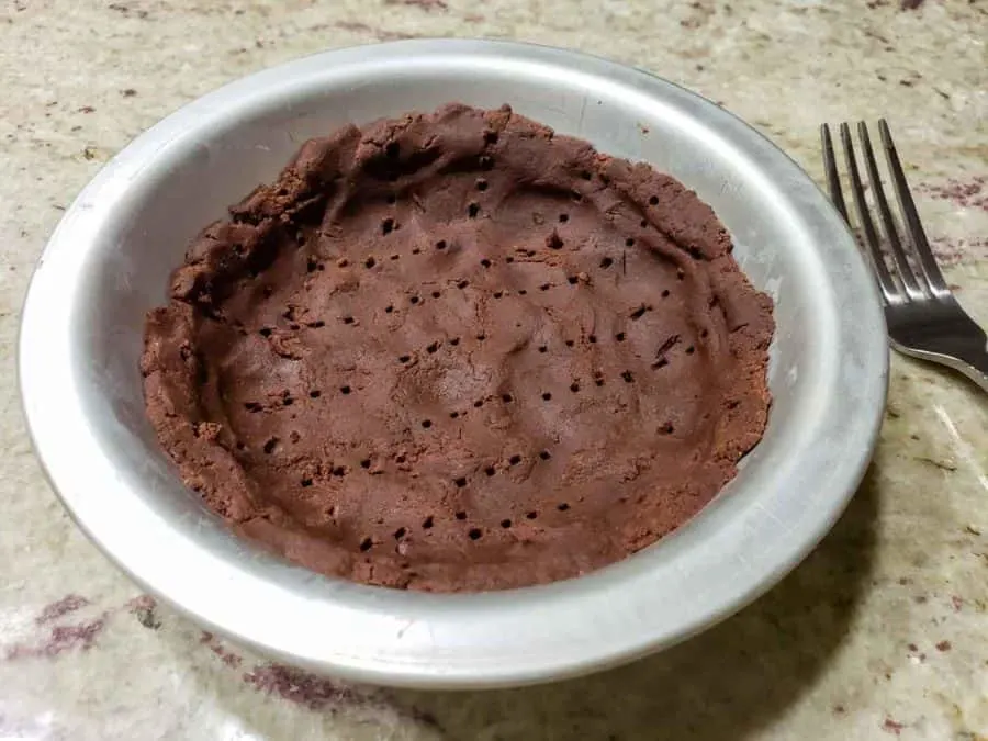a small pie pan filled with chocolate crust with fork holes poked into it.