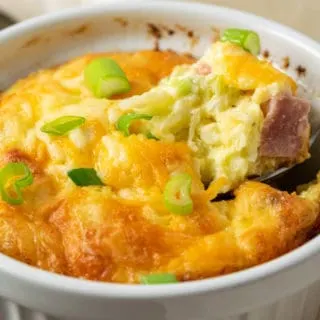 a casserole dish filled with baked egg, ham, cheese, and hash browns with a spoon scooping some up