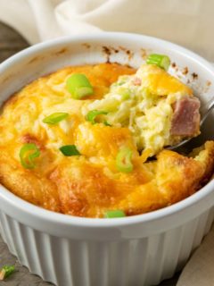 a casserole dish filled with baked egg, ham, cheese, and hash browns and a spoon lifting some out