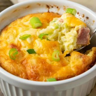 a casserole dish filled with baked egg, ham, cheese, and hash browns and a spoon lifting some out