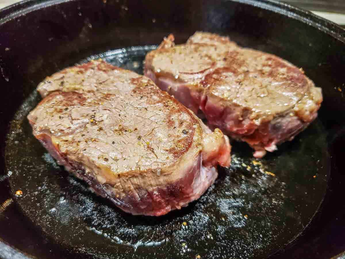 two filet mignon beef tenderloin steaks cooking in a cast iron skillet