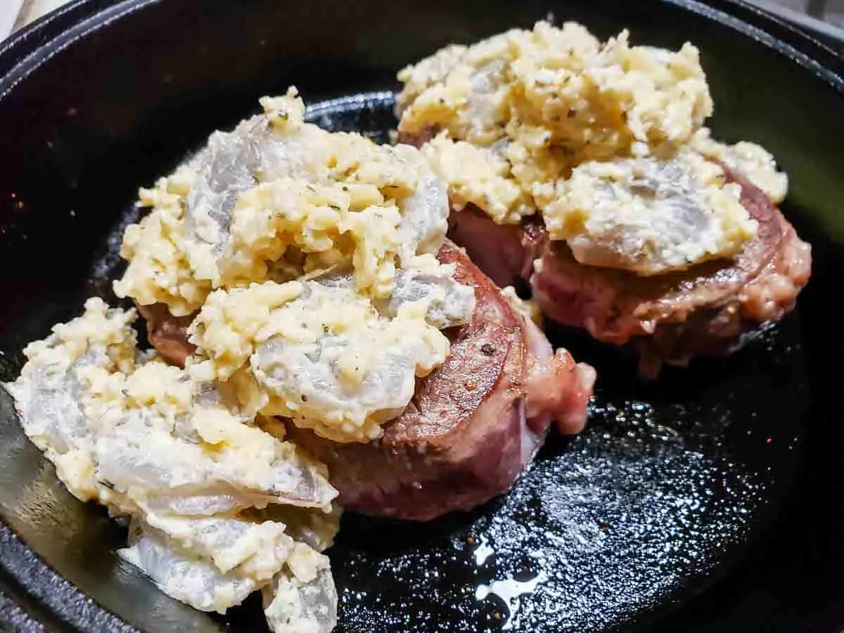 two filet mignon beef tenderloin steaks topped with shrimp and parmesan cheese mixture cooking in a cast iron skillet