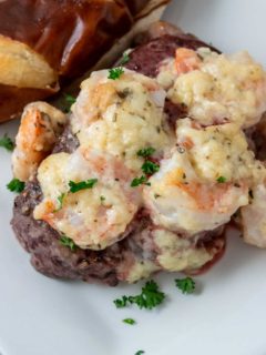 a filet mignon steak topped with shrimp and Parmesan cheese sauce sprinkled with parsley and a side of pretzel baguette