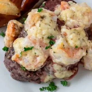 a filet mignon steak topped with shrimp and Parmesan cheese sauce sprinkled with parsley and a side of pretzel baguette