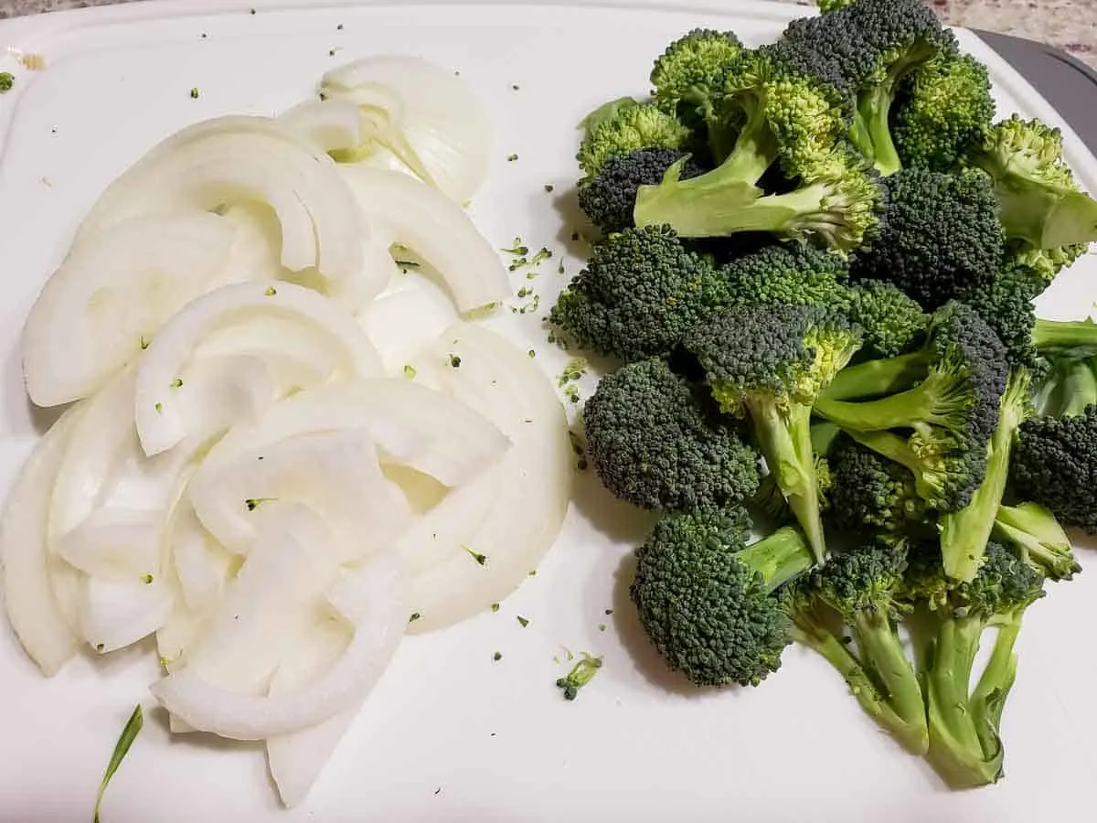 a cutting board with sliced onions and broccoli florets.