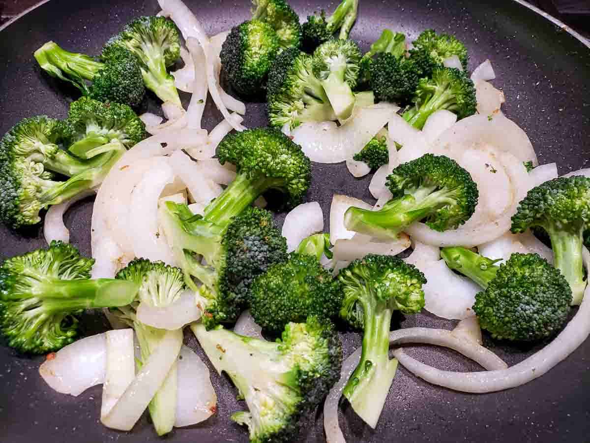 a frying pan filled with onion slices and broccoli florets cooking.