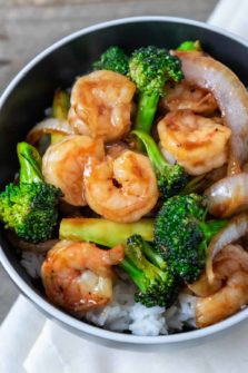 a black bowl filled with white rice, broccoli florets, sliced onions, and shrimp coated in an orange colored sauce