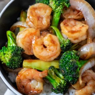 a black bowl filled with white rice, broccoli florets, sliced onions, and shrimp coated in an orange colored sauce