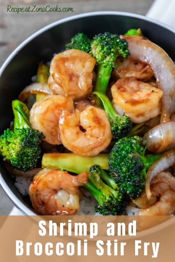 a bowl filled with white rice, broccoli florets, sliced onions, and shrimp coated in an orange colored sauce.