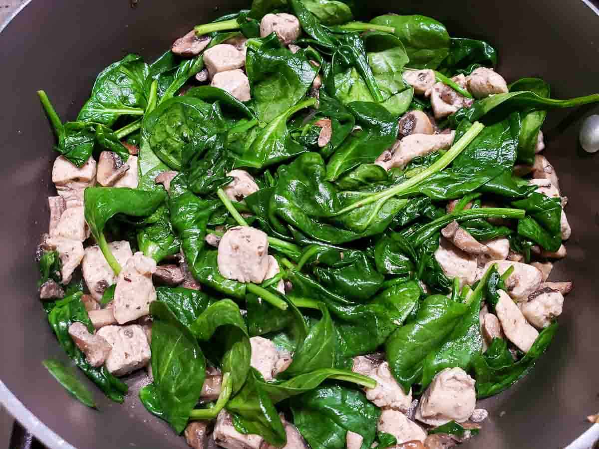 wilted spinach, chicken, and mushrooms cooking in a pan