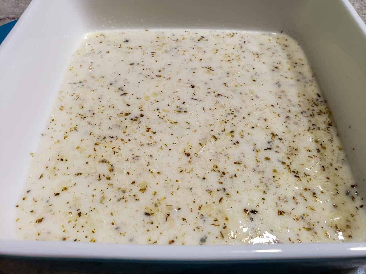 an 8x8 inch casserole dish with white sauce layered on the bottom