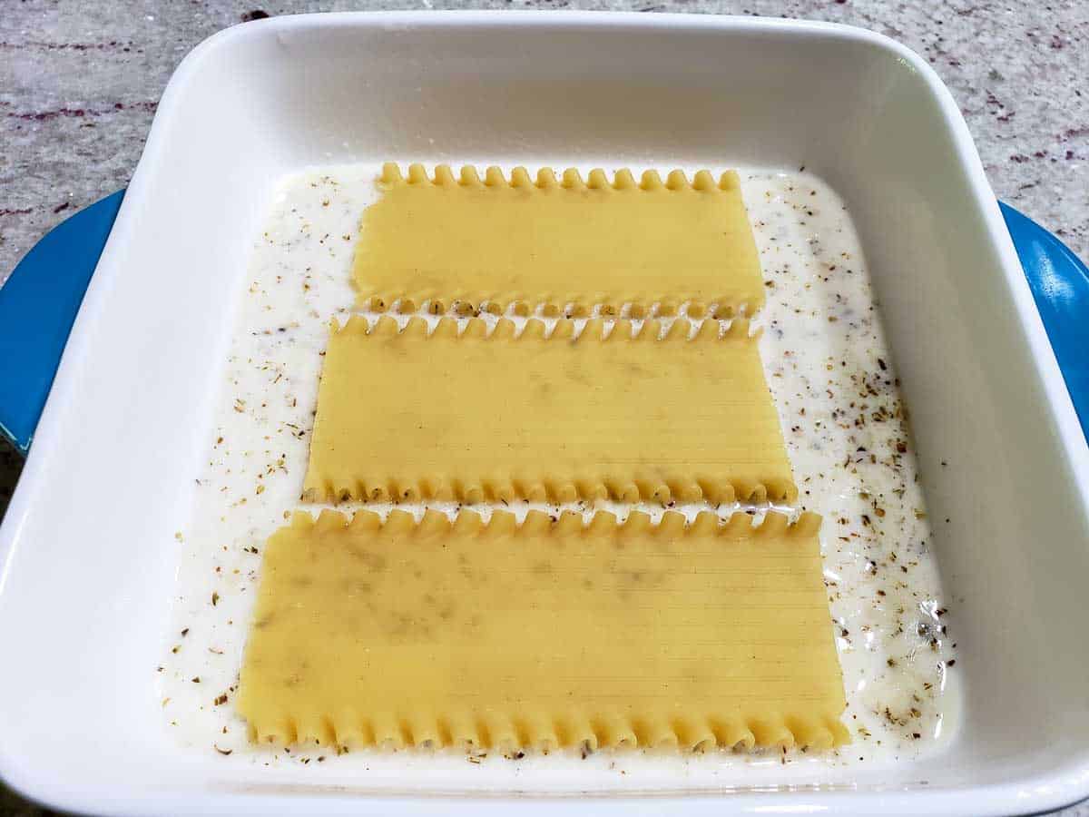 3 half lasagna noodles layered over white sauce in a dish