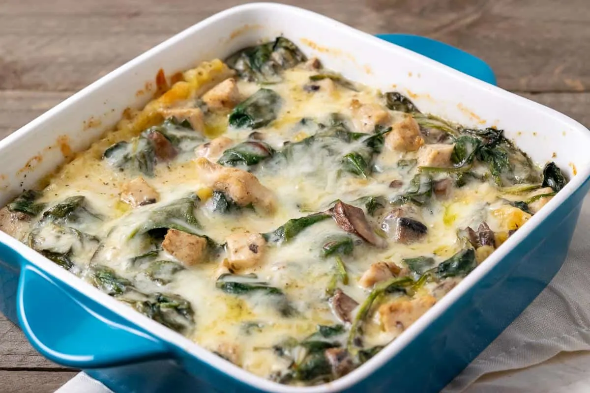 an 8 x 8 casserole dish of baked lasagna filled with lasagna noodles, spinach, chicken, and mushrooms in a white creamy sauce