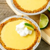 two small yellow pies in graham crusts topped with whipped cream and quarter lime slice.