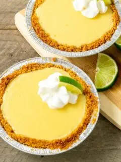 two small yellow pies in graham crusts topped with whipped cream and quarter lime slice.