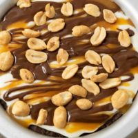 a top down view of a small pie pan filled with chocolate crust, creamy filling, caramel sauce drizzle, chocolate ganache drizzle, and peanuts.